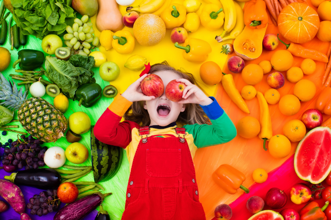 Girl surrounded by fruit using apples as her eyes